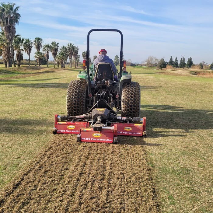 Tractor con una máquina de mantenimiento trabajando sobre el césped del campo de golf
